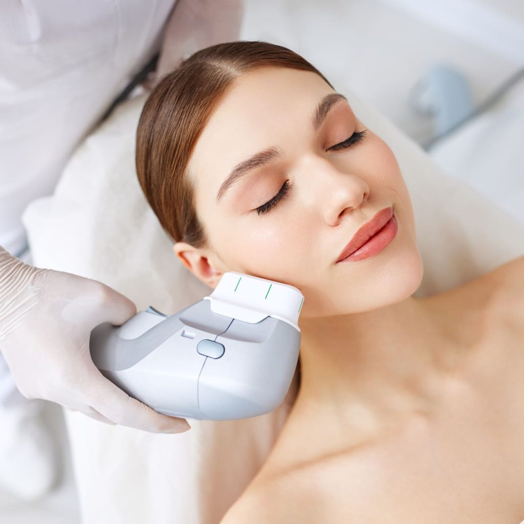 Woman getting facial lifting therapy in beauty salon From above of relaxed young female client getting SMAS ultrasound face lifting massage with professional equipment in beauty center